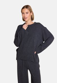 Mørkegrå oversized genser med rund halsutskjæring, vide ermer og ribbestrikkede mansjetter, sammen med matchende, løst sittende bukser.