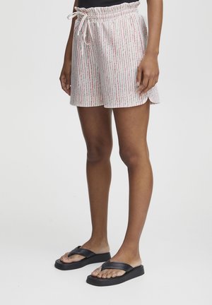 Shorts légers et courts en tissu blanc avec des rayures verticales roses et rouges, dotés d'une taille élastique et d'un cordon de serrage. Associés à des sandales noires.