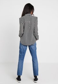 Camicetta a righe bianche e nere con colletto a bottoni, abbinata a jeans in denim blu e sneakers nere, vista da dietro.