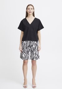 Top in lino nero con maniche corte e scollo a V, abbinato a pantaloni corti fino al ginocchio con una stampa zebratica in bianco e nero. Sandali con tacco argentei.