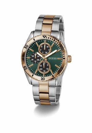 Tofarvet sølv- og guldfarvet metal armbåndsur med grøn urskive, tre sorte underinddelinger, guldfarvede timemarkører og GUESS-logo på højre side.