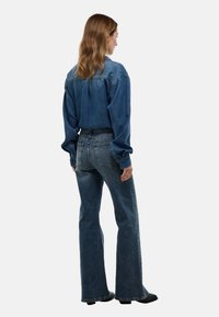 Chemise en denim à coupe ample et à manches longues, associée à un jean flare bleu moyen. La tenue présente des coutures classiques et un design minimal.