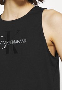 Schwarzes ärmelloses Tanktop aus Baumwolle, mit einem auffälligen Logo in Grau und Weiß. Runder Halsausschnitt mit lockerer Passform und Seitennähten.