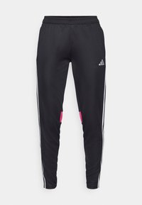 Černé sportovní kalhoty vyrobené z hladkého materiálu, se strukturálními bílými pruhy po stranách, růžovými akcenty na kapsách a logem adidas na stehně.