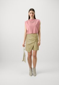 Top senza maniche rosa con collo alto, abbinato a una gonna avvolgente in finta pelle beige con nodo laterale. Stivali alla caviglia grigi e borsa piccola.