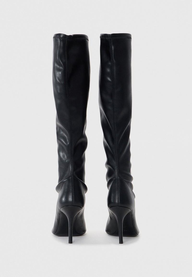 Schwarze Lederstiefel bis zum Oberschenkel mit einer taillierten Form, spitzer Zehenpartie und Stiletto-Absatz. Glatte Textur und sichtbare Nahtdetails.