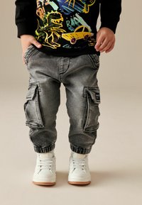 Pantalones cargo grises con puños elásticos y bolsillos laterales, combinados con zapatillas blancas con suela de goma. Sudadera gráfica negra por encima.