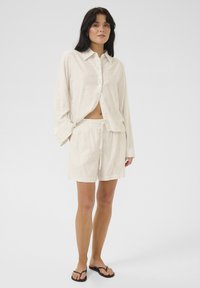 Lahkotna loungewear postava s kremnofarbnimi črtami, ki vključuje srajco z dolgimi rokavi na gumb in kratke hlače z elastičnim pasom in vrvico.