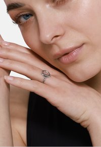 Zilveren ring met een geometrisch ontwerp met een circulair element en een horizontale band, weergegeven op een hand met een natuurlijke nagellak.