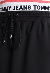 Svarta sportshorts med elastisk midja och röda och vita randiga detaljer. Inkluderar en svart dragsko för justerbar passform.