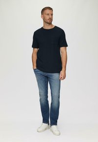 Navyblaues Kurzarmhemd mit Tasche, kombiniert mit hellblauen Jeans und weißen Turnschuhen. Einfacher, lässiger Stil mit lockerer Passform.