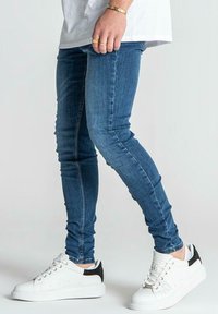 Skinny blue denim jeans with a smooth texture, paired with white sneakers featuring black accents and a chunky sole.