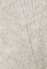 Ljust grått stickat tyg med en mjuk, texturerad yta som har ett diagonalt mönster. Garnet verkar ulligt och något fluffigt.