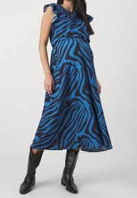 Sininen ja musta zebra-kuvioinen midimekko, jossa on röyhelöhuulet ja nauhakiinnitys, valmistettu kevyestä kankaasta. Yhdistetty polvipitkiin mustiin saappaisiin.