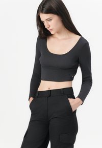 Top cropped negru cu model rib, gât decupat și mâneci lungi, asortat cu pantaloni negri cu talie înaltă, care au buzunare laterale.