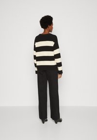 Maglione a righe bianche e nere con vestibilità morbida. Tessuto a maglia, maniche ampie e scollatura rotonda. Abbinato a pantaloni neri a vita alta.