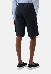 Mørkeblå cargo shorts med afslappet pasform, elastisk talje og en baglomme med lynlås. Båret med mørkeblå slip-on sko.