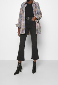 Camicia over-size a quadri multicolore, top aderente nero, jeans neri svasati e stivaletti neri con punta. Tessuti a texture e pattern contrastanti.