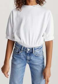 T-shirt bianco in cotone con maniche corte e orlo arricciato. Abbinato a jeans in denim blu chiaro con chiusura a bottoni e tasche.
