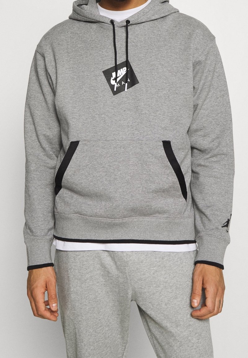 Homme portant un sweat à capuche Nike Jumpman gris et un pantalon de survêtement assorti avec des poches et des cordons de serrage bordés de noir.
