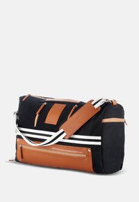 Black canvas duffel bag with brown leather accents, white stripes, multiple zippered pockets, and a detachable shoulder strap.