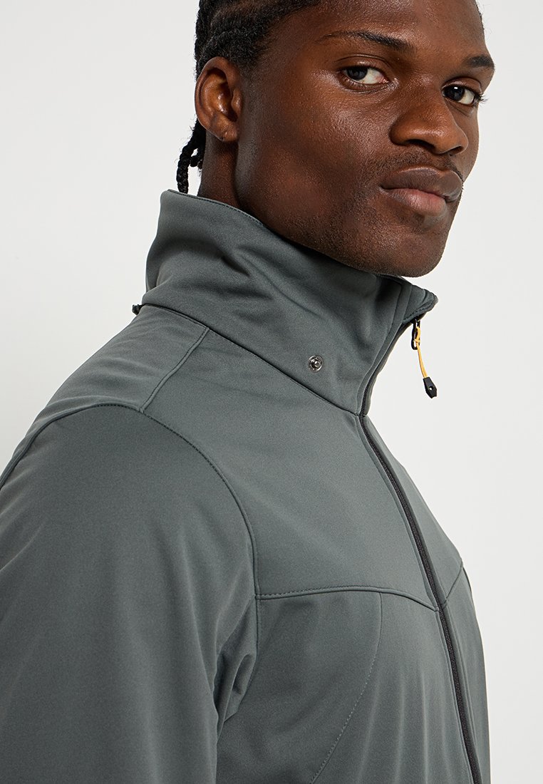 Veste grise zippée avec col haut, confectionnée dans un tissu lisse et extensible. Présente un tirette de fermeture éclair jaune et un détail à pression au col.