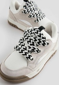 Baskets en suède gris et mesh blanc avec des lacets zébrés noir et blanc, semelle en caoutchouc, bout rond et accents latéraux discrets.