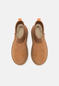 Paire de bottines en daim beige avec garniture en cuir marron, languettes de traction orange et doublure polaire douce couleur crème, vues de dessus sur fond blanc.