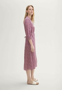 Maxikleid mit Blumenmuster in Pink und Weiß, mit Dreiviertelärmeln, einem Taillengürtel und einer fließenden Silhouette. Getragen mit Sandalen mit breiten Riemen.
