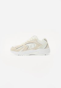 Beige en witte sportschoen van suede en mesh materialen, met een ronde neus, veters en textuuraccenten aan de zijkanten.