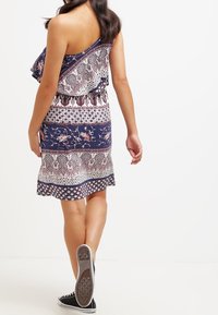 Vestido de rayas en azul marino y blanco con hombros con volantes, cintura elástica y dobladillo acampanado. Combinado con zapatillas negras.