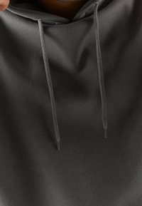 Felpa con cappuccio grigia scura con una texture liscia, dotata di due cordini e una tasca frontale. Cuciture di qualità e dettagli di design minimal.