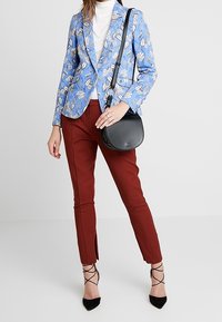 Light blue floral blazer over a white turtleneck, paired with rust-colored tailored pants. Black handbag and strappy black heels complete the look.
