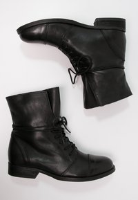 Bottes lacées noires en cuir à la finition lisse, bout rond, petit talon bloc, et lacets décoratifs à l’avant. Dessus au design texturé.