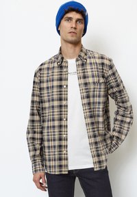 Plaid shirt in beige, navy, and light blue, featuring button closure, long sleeves, and a relaxed fit, layered over a white graphic t-shirt.
