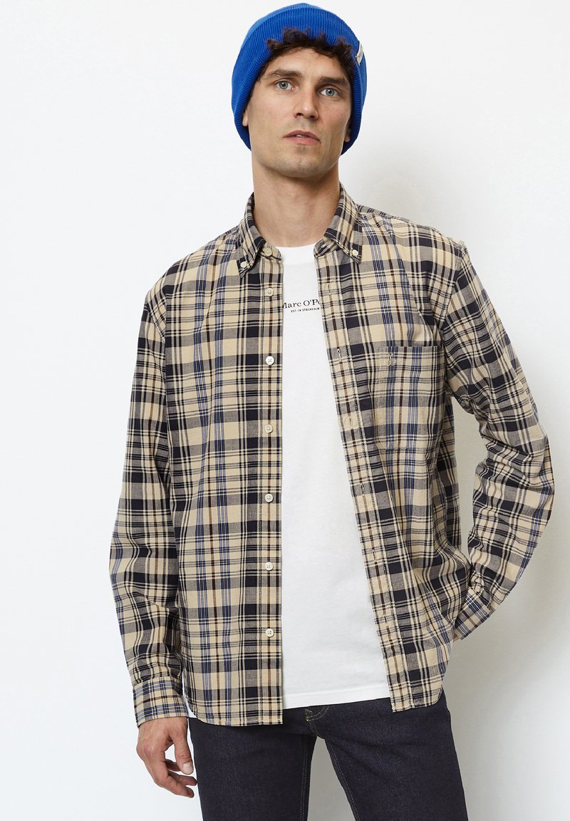 Plaid shirt in beige, navy, and light blue, featuring button closure, long sleeves, and a relaxed fit, layered over a white graphic t-shirt.