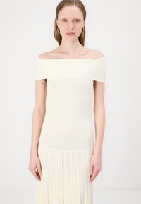 Haut crème ajusté, sans manches, en tissu doux, avec une texture lisse. Le design présente une silhouette flatteuse et un minimalisme dans les détails.