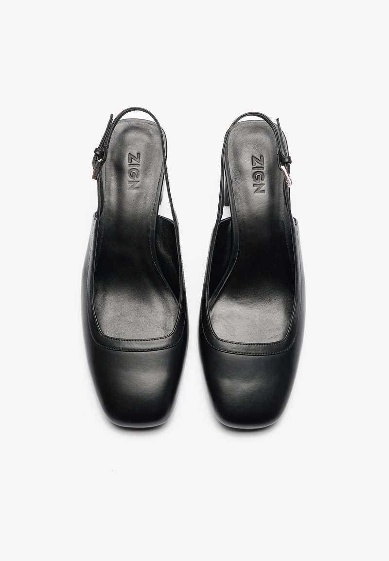 Scarpe slingback in pelle nera con punta quadrata, texture liscia e cinturino largo. Logo stampato sulla soletta. Nessun hardware visibile.