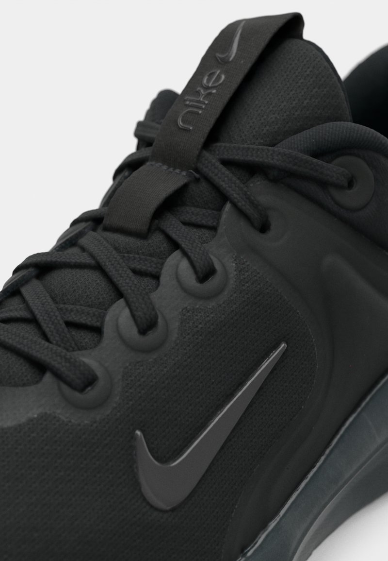 Acercamiento a una zapatilla negra de Nike que muestra la tela texturizada, los cordones y el logo de swoosh de Nike en el lateral.