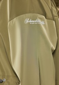 Olive green, lightweight rain jacket with a smooth texture. Features a logo embroidered in white on the upper sleeve.