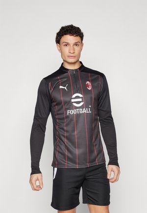 Black long-sleeve football shirt with red stripes, Puma logo on chest, zipper collar, and "Football" printed on front. Worn with black shorts.