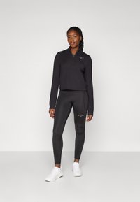 Top cropped nero a maniche lunghe con mezza zip e leggings abbinati a vita alta. Accenti di logo bianchi e tessuto liscio ed elastico. Sneakers bianche.