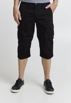 Black cargo shorts with a relaxed fit, featuring side pockets, knee-length cut, and a textured cotton material. Worn with black sneakers.