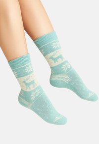 Legs wearing light blue winter socks with white patterns of a reindeer, bear, and snowflakes on a plain background.
