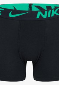 Black boxer shorts made of soft fabric with a wide green Nike-branded elastic waistband featuring a logo and pattern detail on top.