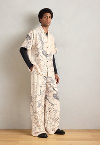 Beige short-sleeve shirt and wide-leg pants featuring a black map outline pattern, made from lightweight fabric, paired with black shoes.