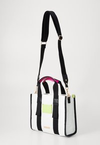 Weiße und schwarze Tragetasche mit strukturiertem Muster, schwarzen Griffen, einem rosa Akzent im Inneren und einem grünen Etikett an der Seite.