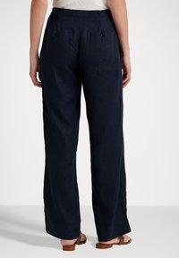 Tmavě modré široké kalhoty z texturované látky, s dvěma zadními kapsami na knoflíky a volným střihem.