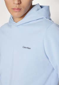 Felpa con cappuccio di colore azzurro chiaro realizzata in morbido cotone, con un piccolo logo nero "Calvin Klein" sul petto.