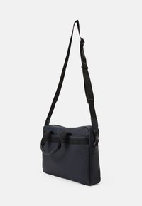Bolso mensajero de un oscuro color marino con una textura suave, doble asa en la parte superior, correa de hombro ajustable y un bolsillo frontal plano con cremallera.